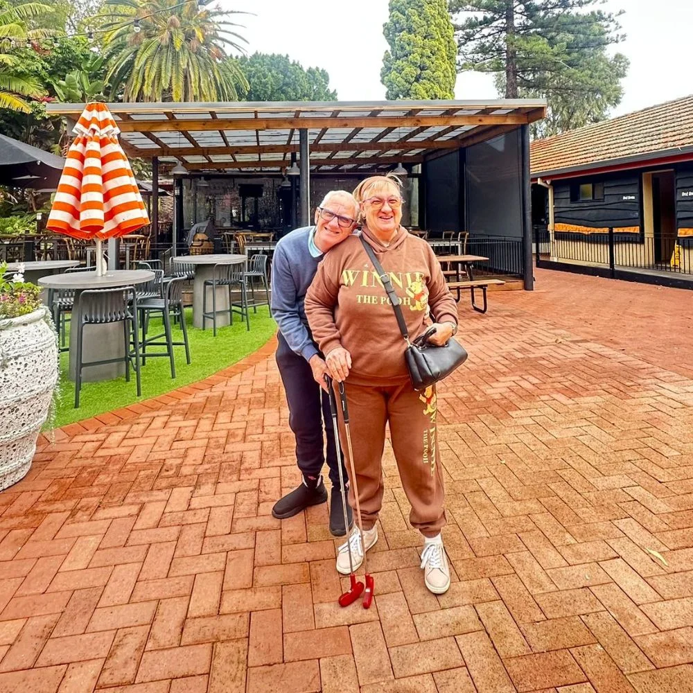Two people walking together outdoors, one using a walking stick for support