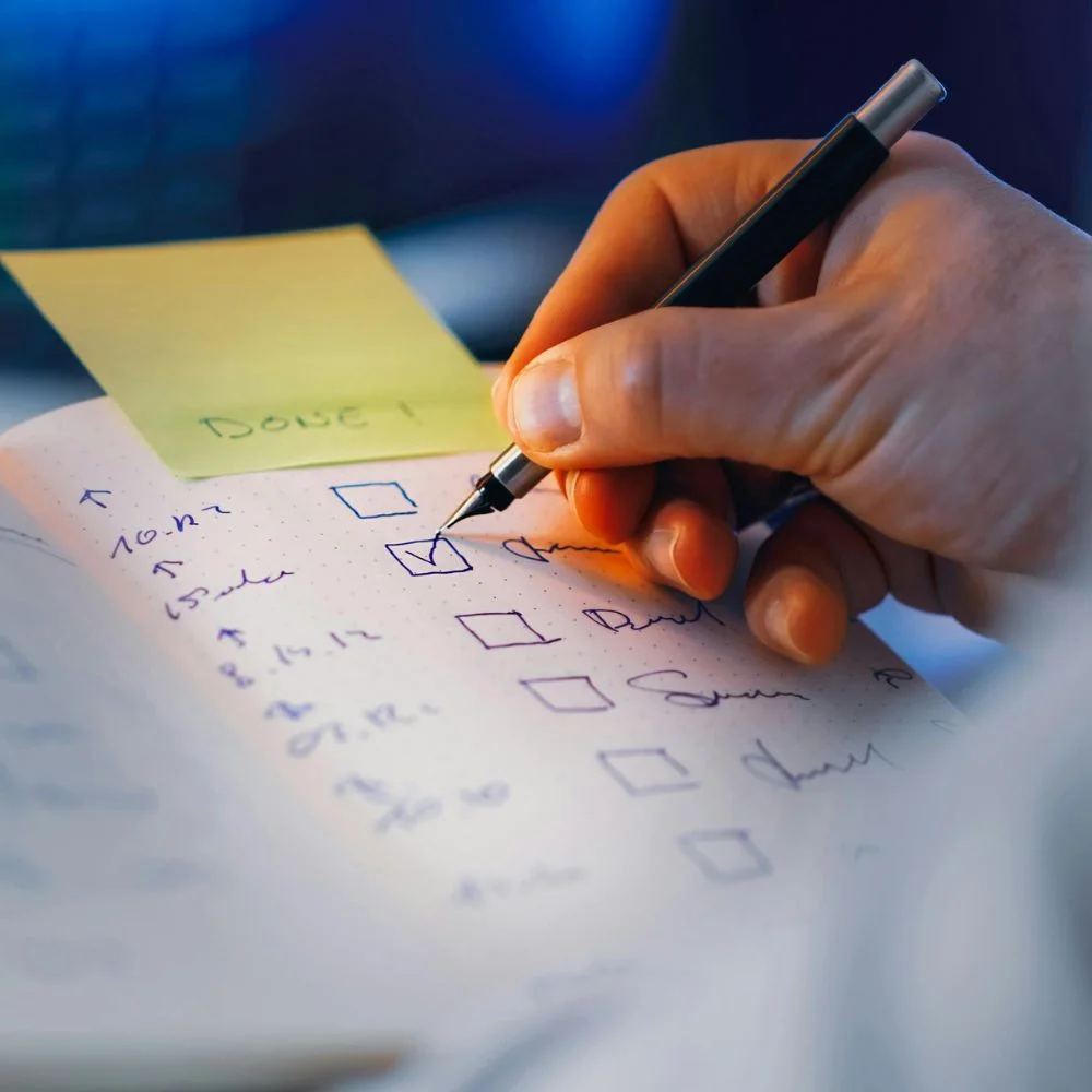 A hand ticking checkboxes on a handwritten list with a fountain pen