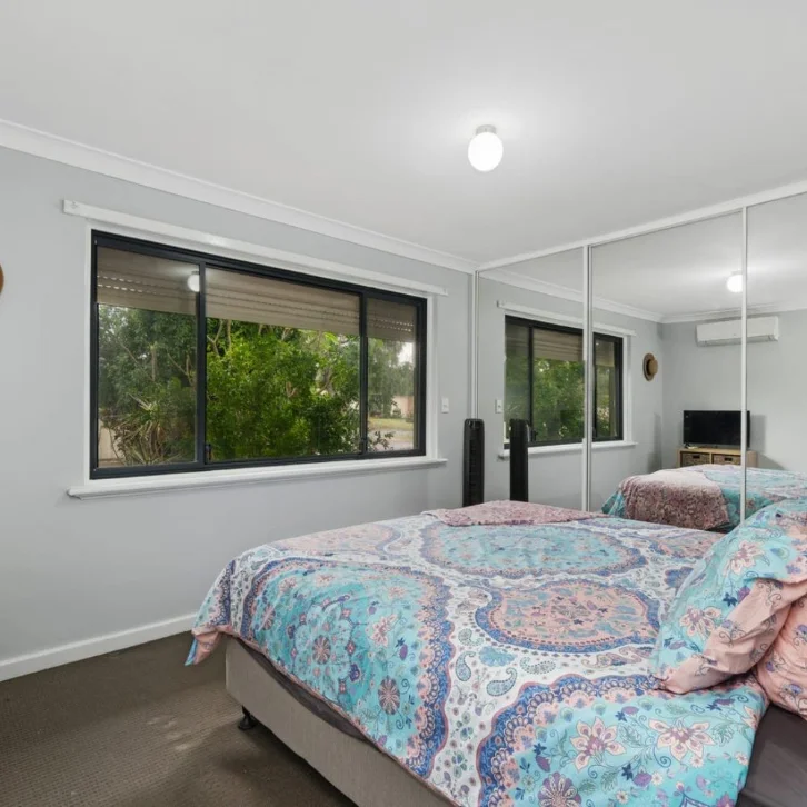 A furnished bedroom with a large window and mirrored wardrobe