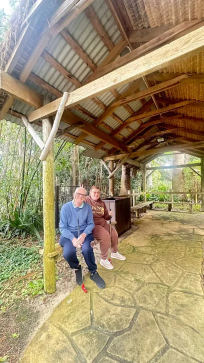 Two people sitting together under a timber shelter in a bush setting