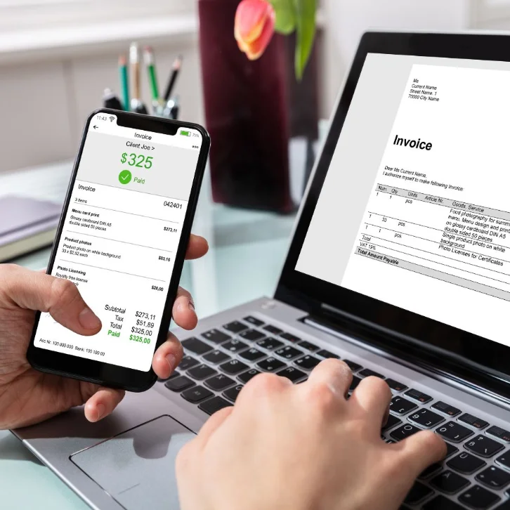 Hands using a laptop and mobile phone to process an invoice